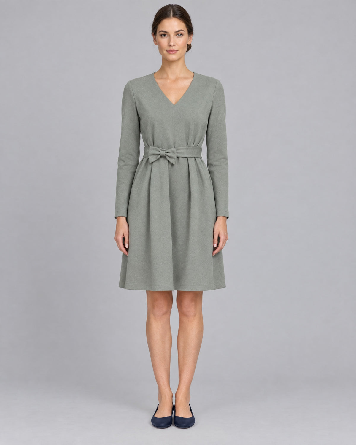 A woman wearing a sage gray-green long-sleeve V-neck Punto Milano dress, knee-length A-line skirt, front view, full length, studio. #Color_Gray green