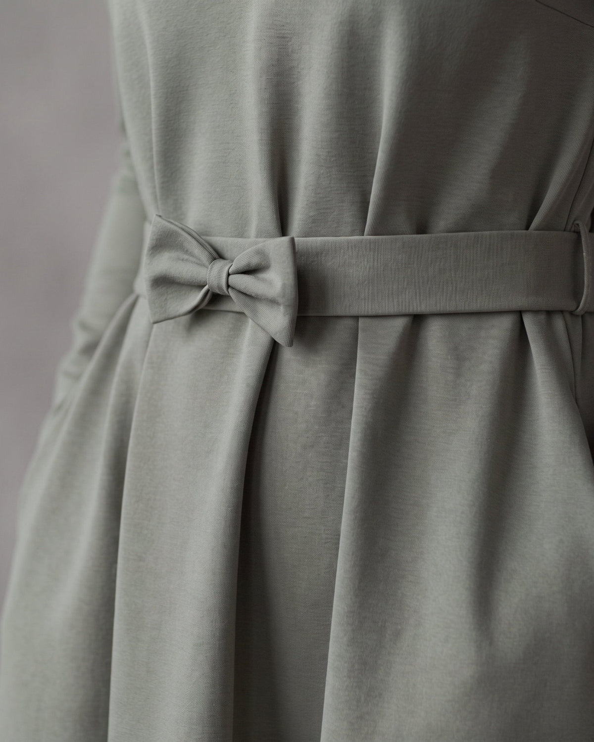 A sage green dress with a matching fabric tie belt at the waist, showing the draped skirt and side pocket detail. #Color_Gray green