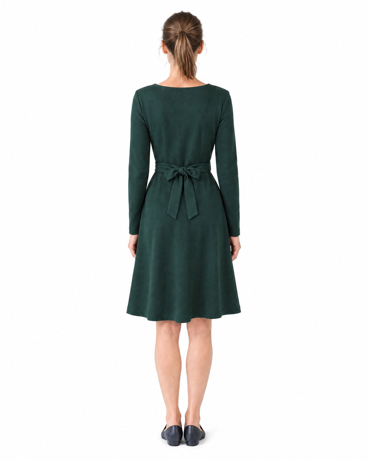A woman wearing a dark green long-sleeve V-neck Punto Milano dress with a tie belt bow, back view, full length. #Color_Green