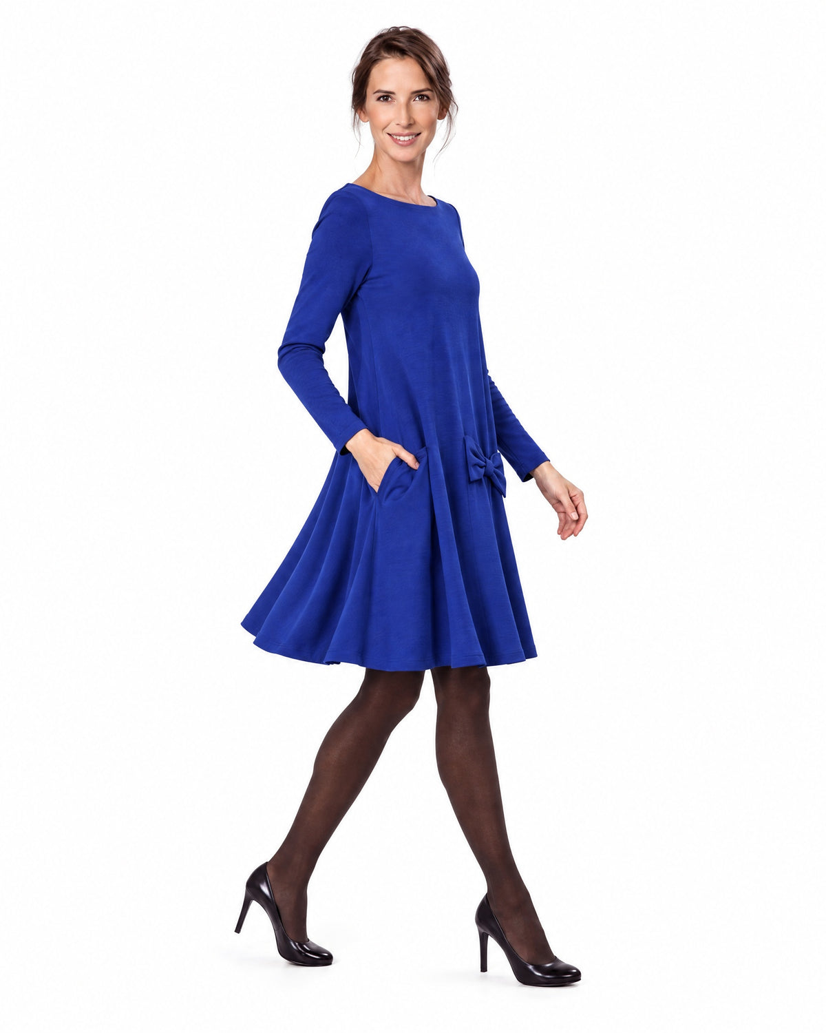 A woman modeling a sapphire blue long-sleeve A-line dress with a boat neckline and bow-detail pocket, shown in profile while walking. #Color_Sapphire blue
