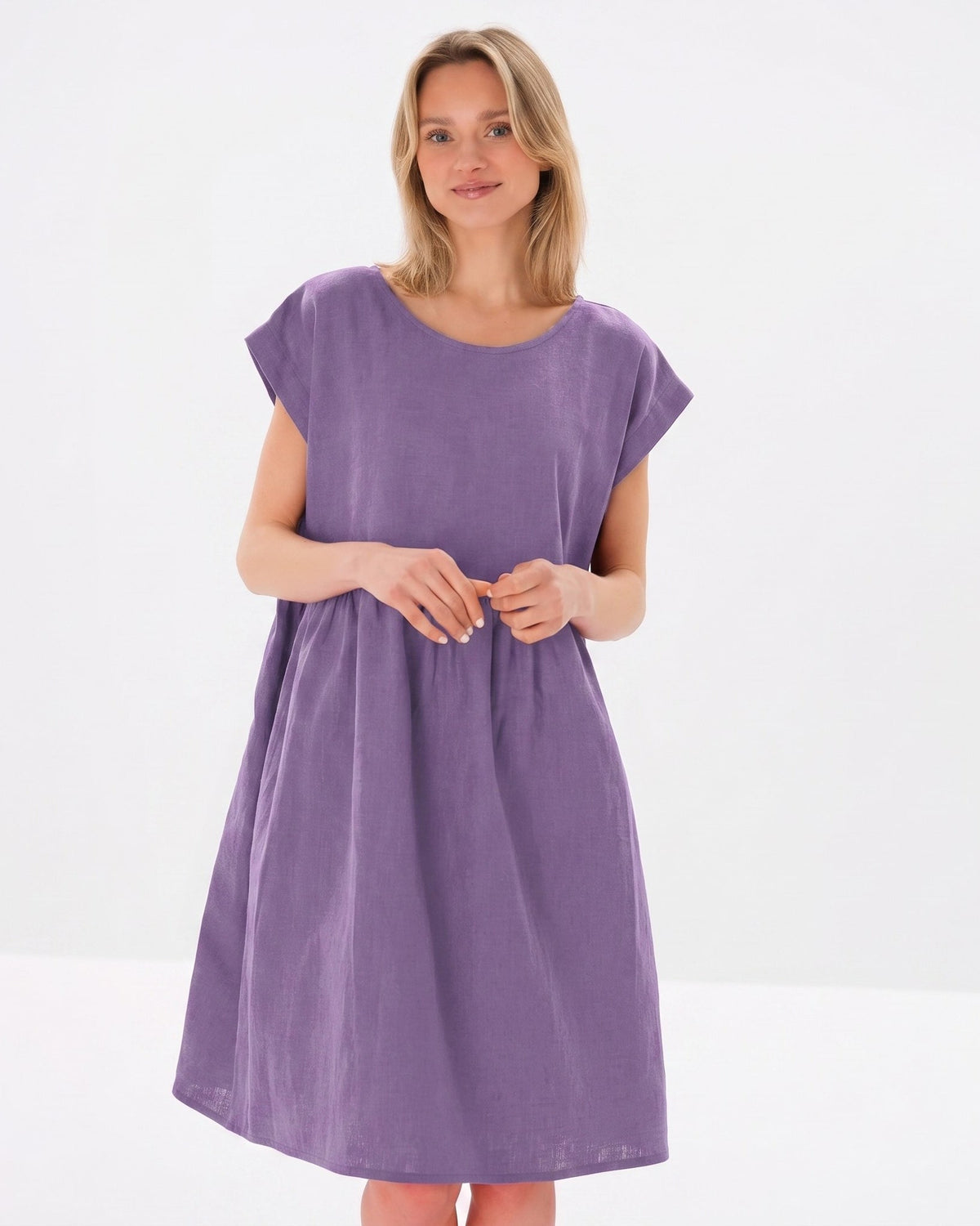 Kvinna visar en ledig, kortärmad lila klänning mot en ren vit studiobakgrund. #Color_Purple