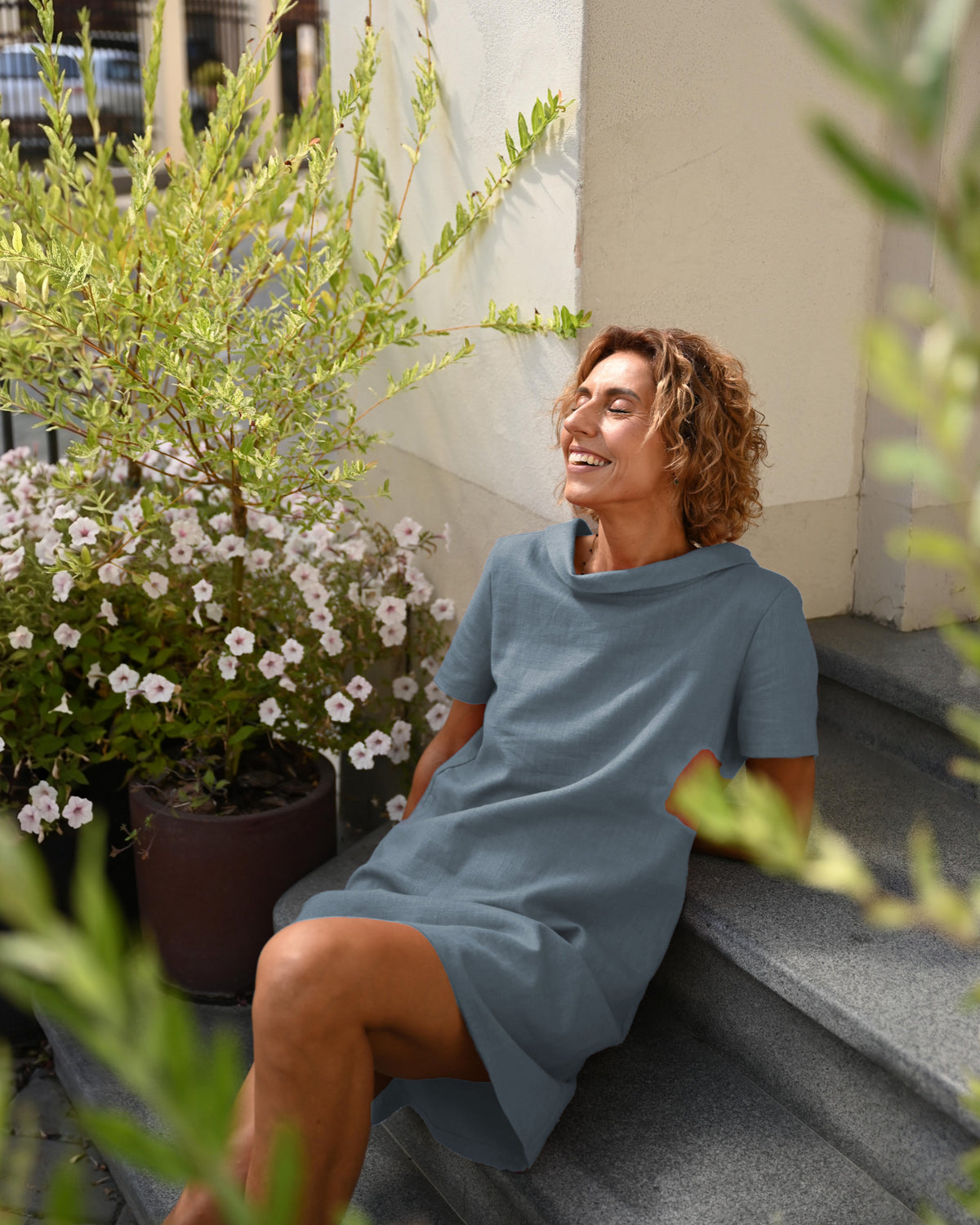 LeMuse STORY linen dress in blue – seated by potted plants #Color_Blue
