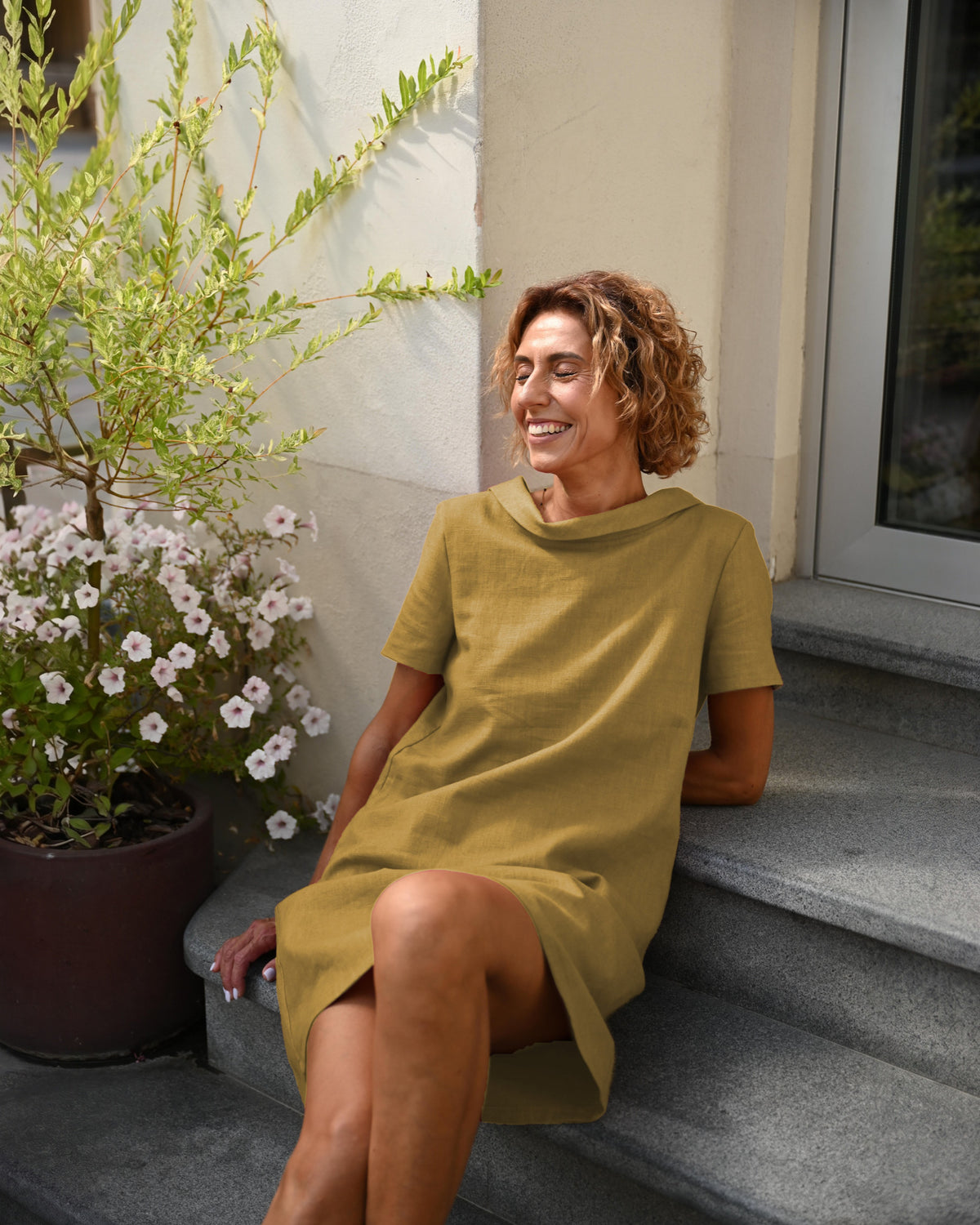 LeMuse STORY linen dress in ochre – seated by potted flowers #Color_Ochre