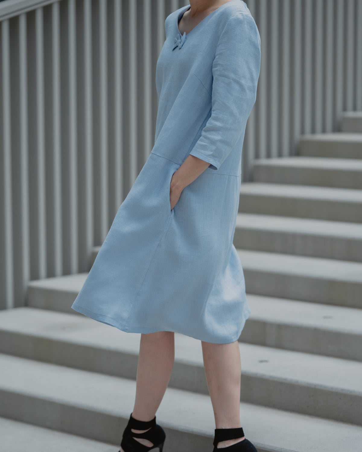 SUN – Linen Blend V-Neck Bow Dress – Light blue dress, three-quarter view with hand in pocket, on stairs #Color_Light blue