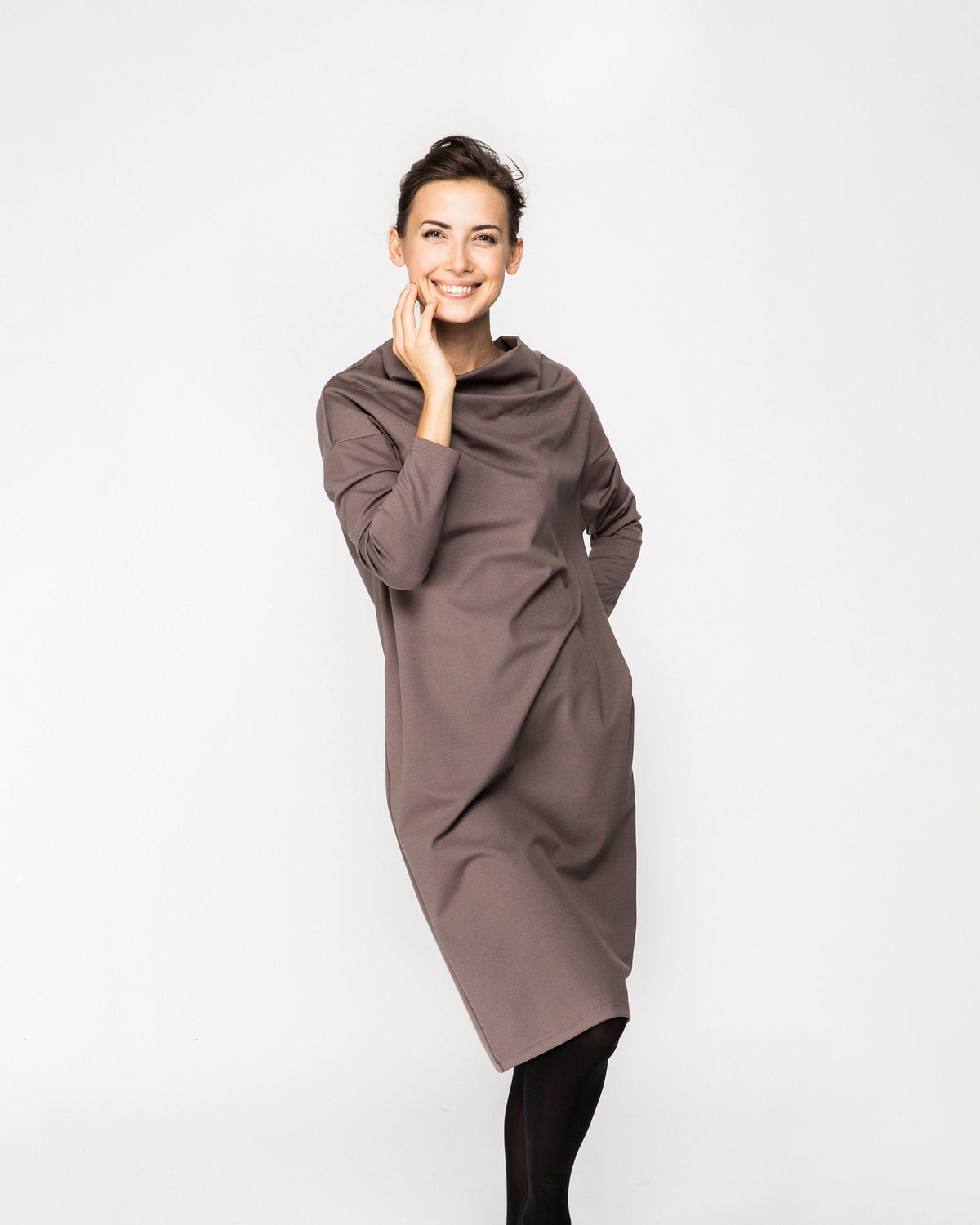 A woman wearing a taupe brown long-sleeve cowl-neck midi dress with side pockets, standing against a white background, front view. #Color_Cacao