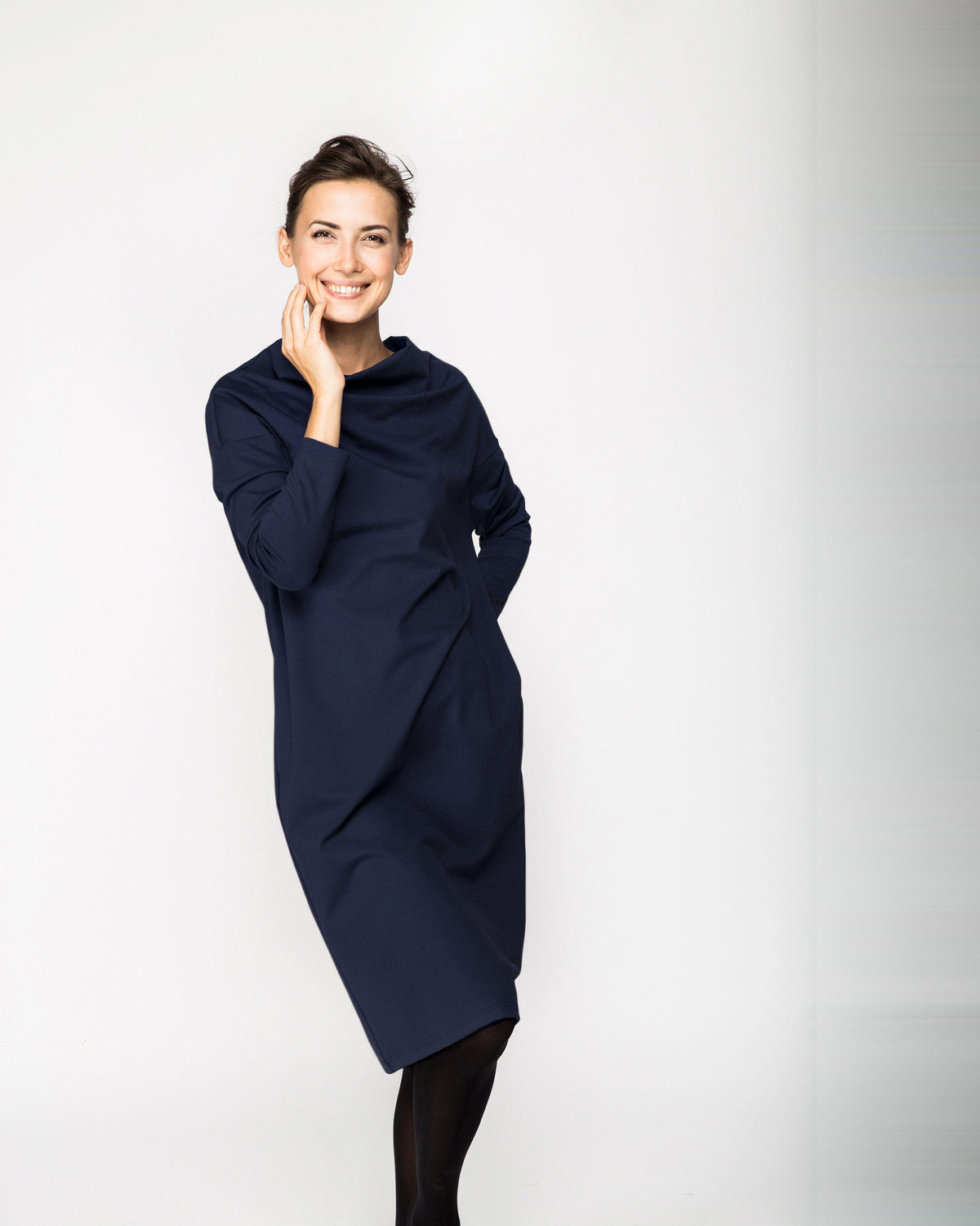 A woman wearing a navy blue long-sleeve cowl-neck midi dress with side pockets, standing against a white background, front view. #Color_Deep blue