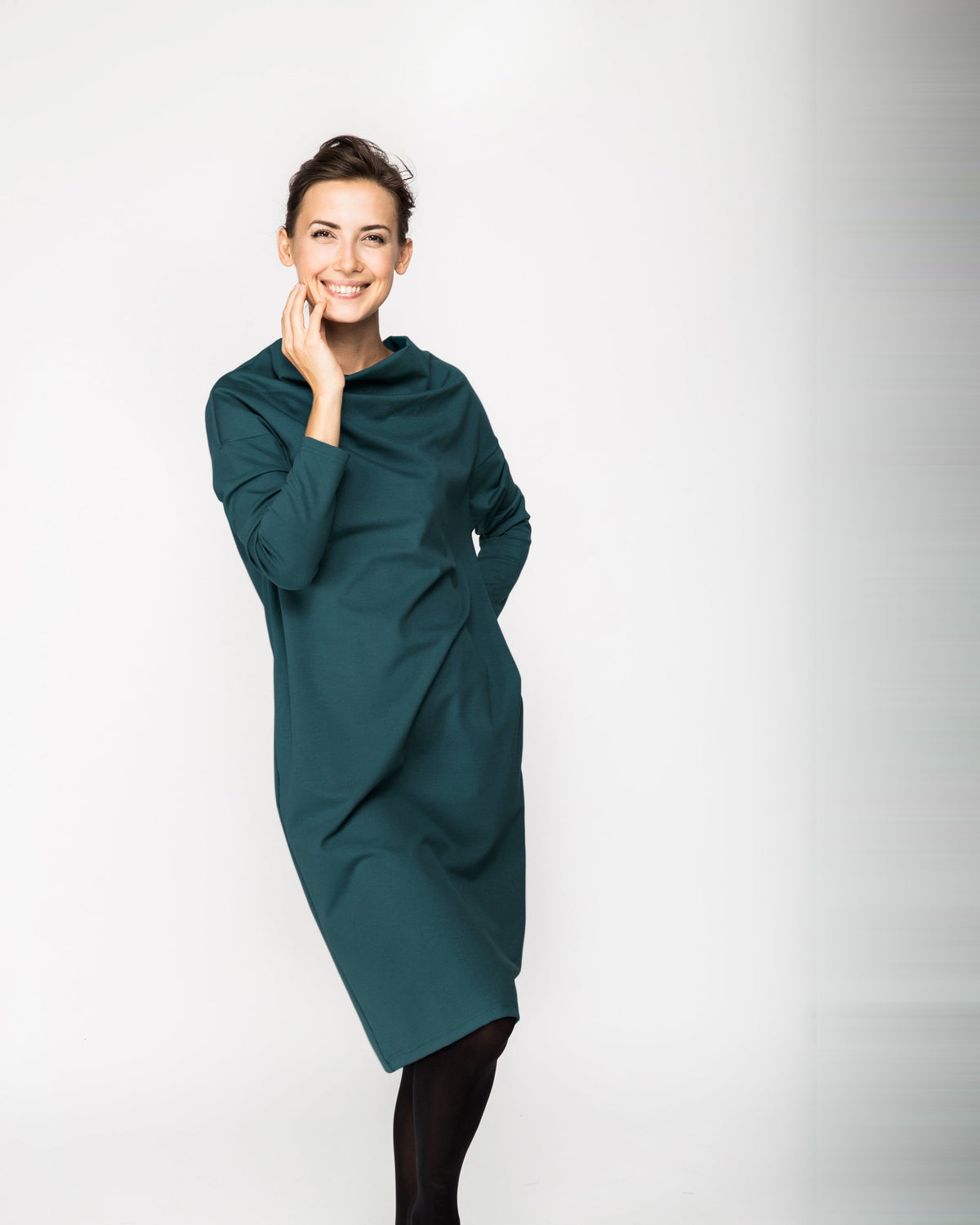 A woman wearing a dark green long-sleeve cowl-neck midi dress with side pockets, standing against a white background, front view. #Color_Green